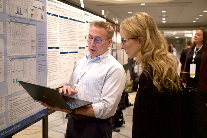 Two TMF2023 attendees looking at laptop in front of research posters