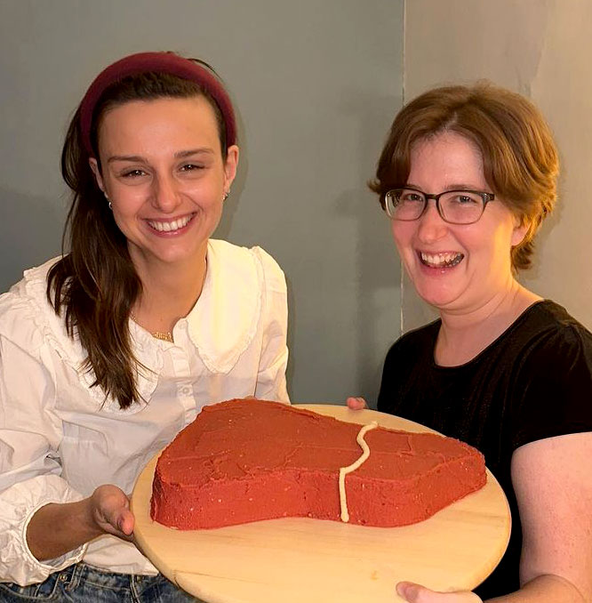Vicky and Zoe holding a cake in the shape of a liver