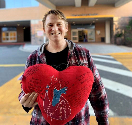 Joey leaving hospital, smiling and holding a pillow with signatures and anatomical heart illustration