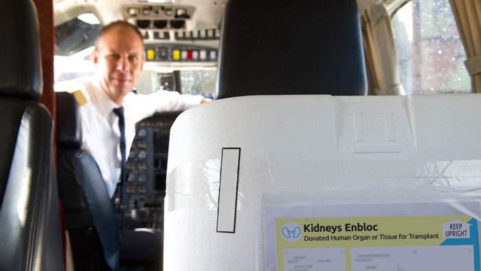 Organ shipment with Kidneys Enbloc label in cockpit of airplane with pilot seated in background, soft focus