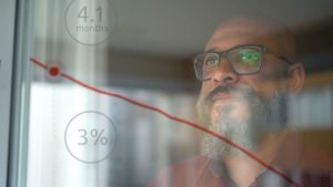 Man with pensive expression looking out window with overlay of 2 circles and a red line from predictive analytics graph