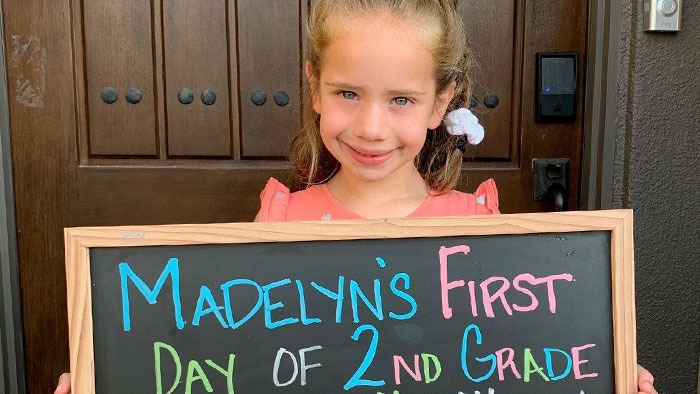 Madelyn, pediatric heart transplant recipient, holding chalkboard sign announcing her first day of 2nd grade