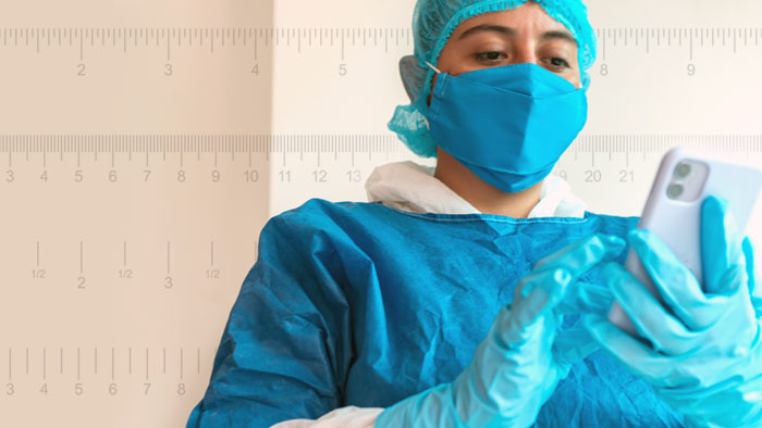 Healthcare provider wearing personal protective equipment while using mobile device. Background of 4 different measurement rulers running across width of image.