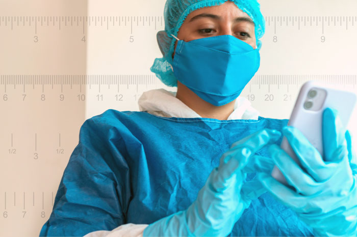 Healthcare provider wearing personal protective equipment while using mobile device. Background of 4 different measurement rulers running across width of image.